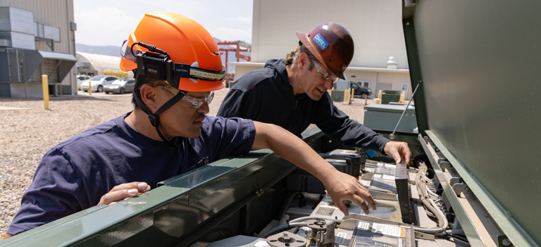 Two people wearing safety gear manipulate objects within a large open container.