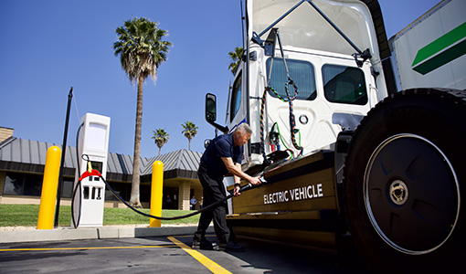 Continue reading about A driver plugs a large white semi-truck cab into an electric charging station.