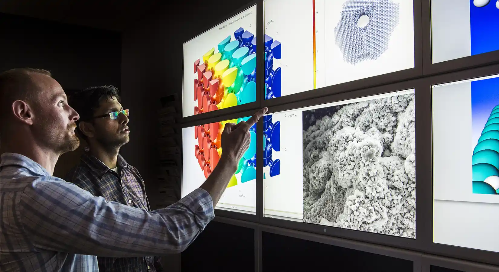 Two researchers facing a wall of computer monitors in a lab.
