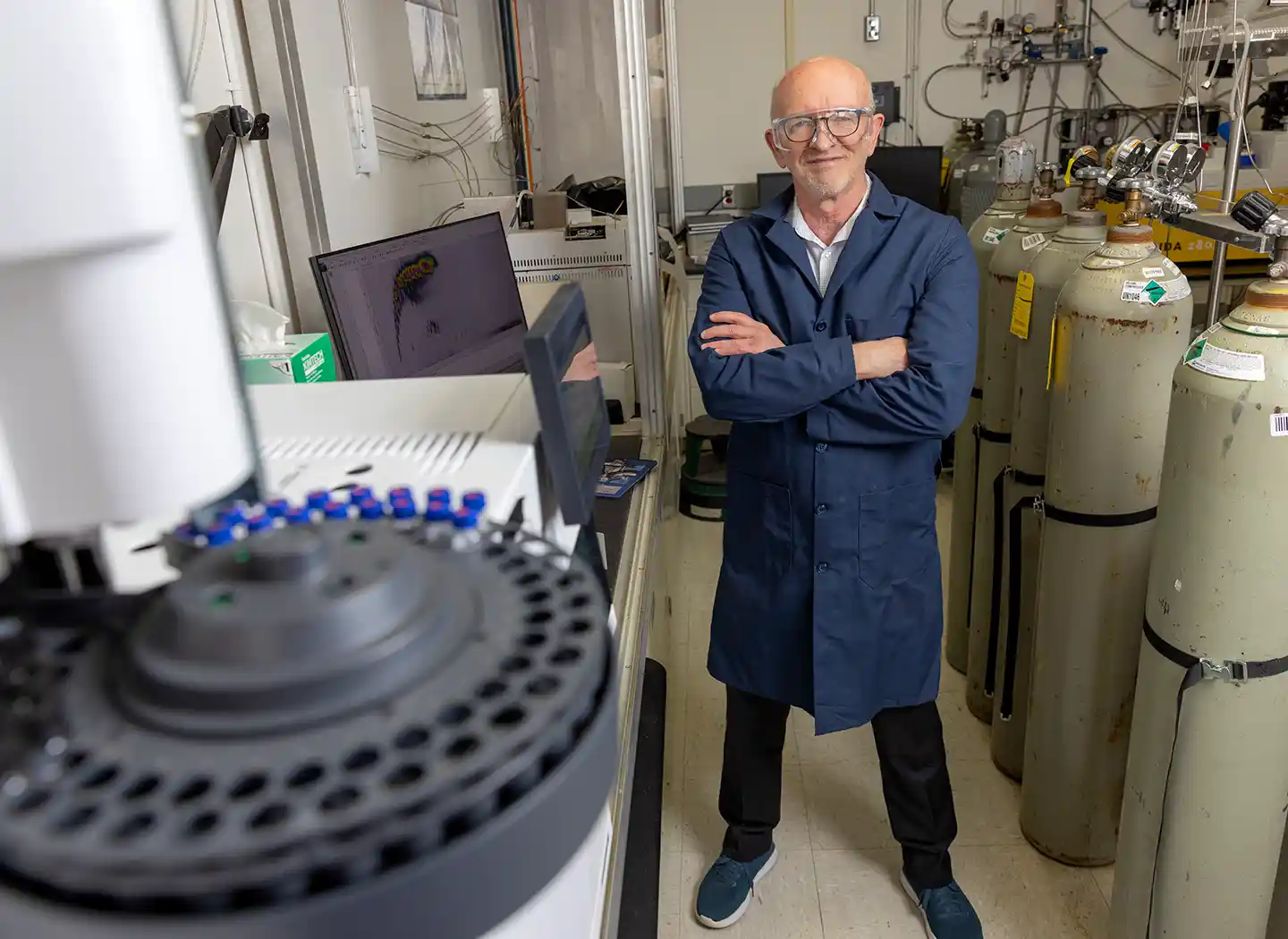 A person stands with their arms crossed next to a 2D gas chromatograph coupled to a time-of-flight mass spectrometer