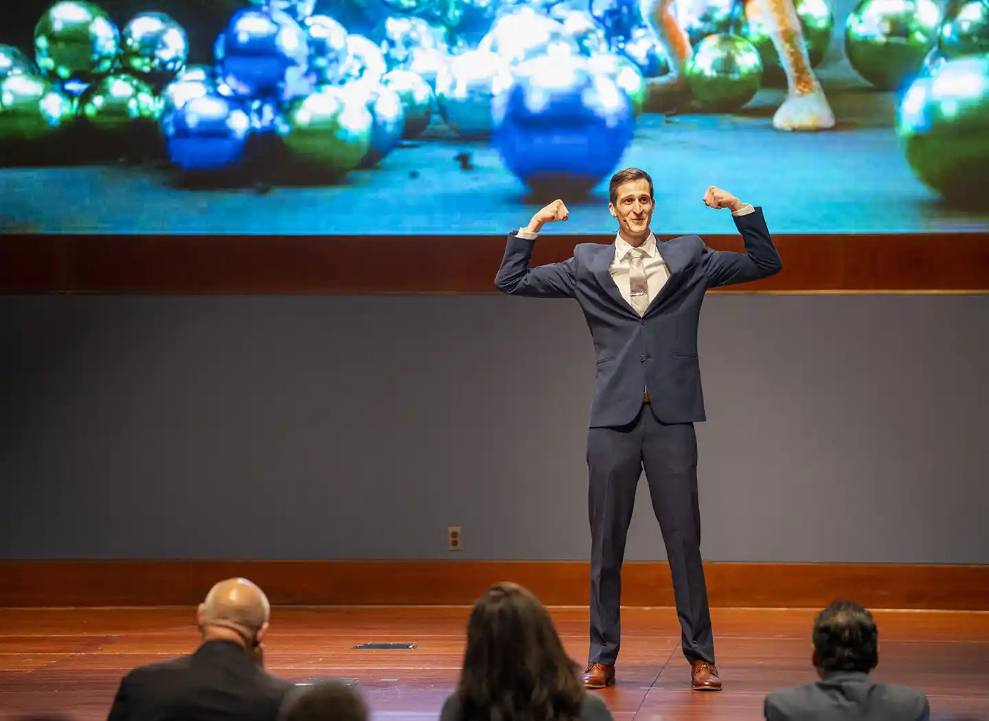 A man in a suit flexes his arms on stage.
