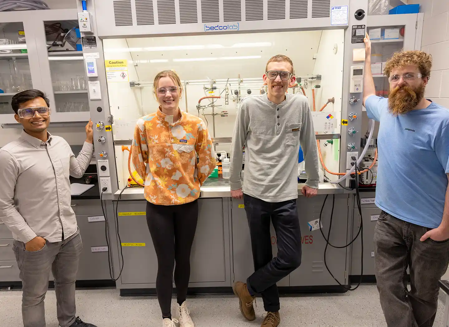 Four people stand in front of laboratory equipment.
