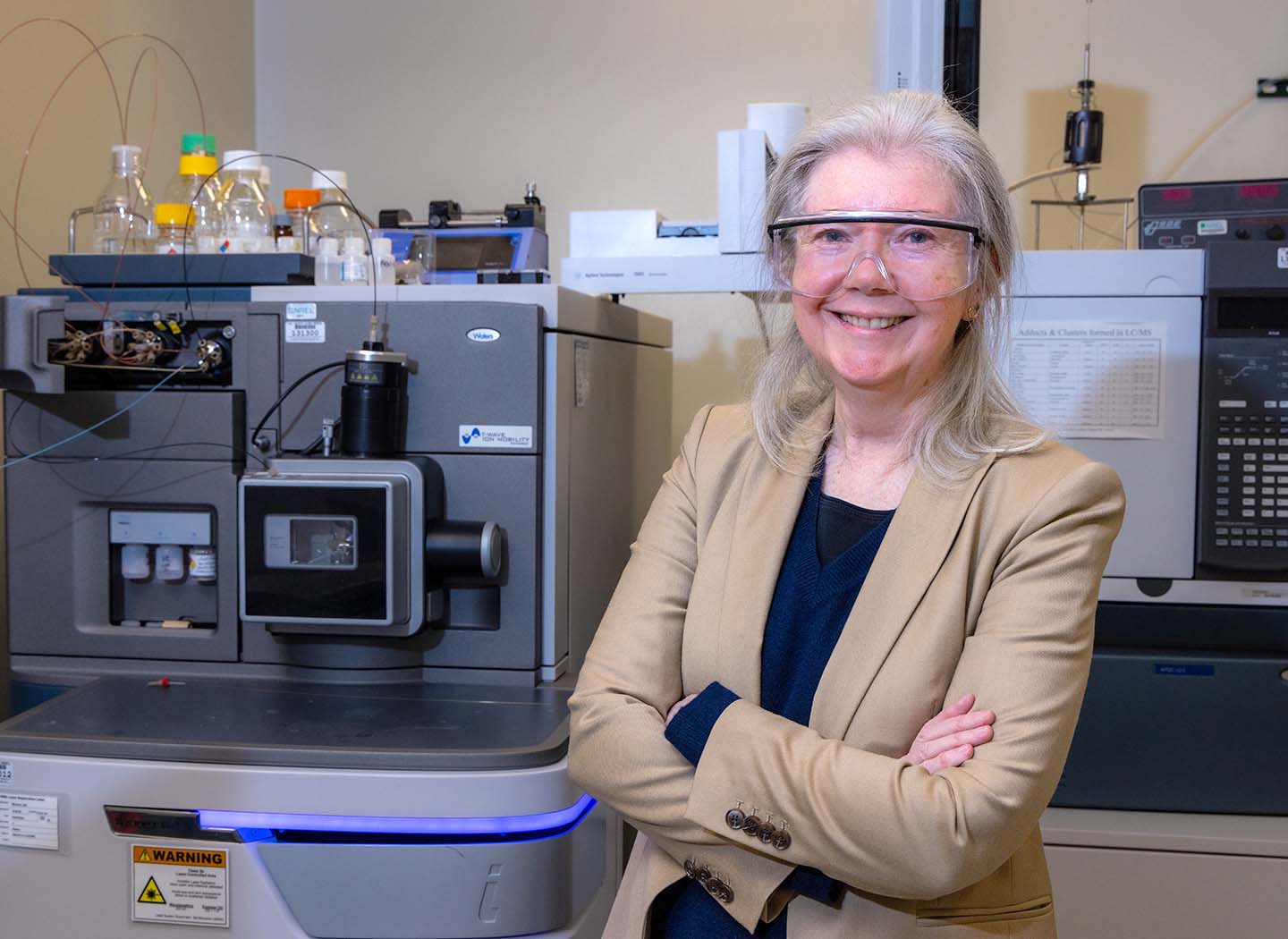 A person wearing safety goggles poses with their arms crossed in a lab.