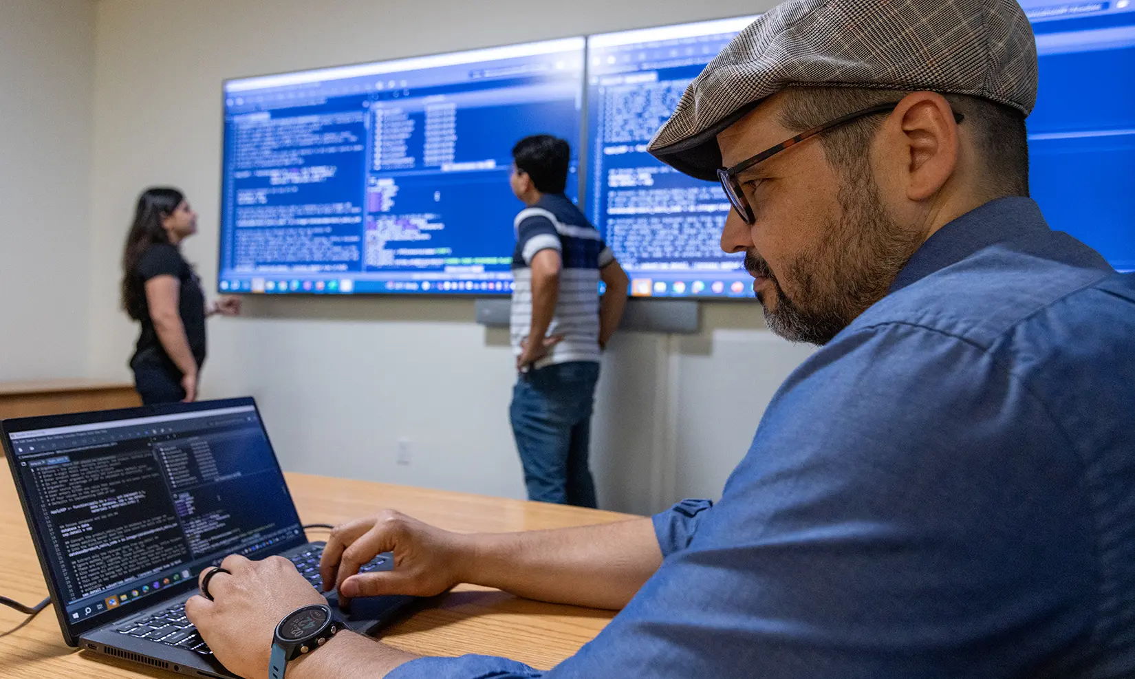 Two researchers examine data on large wall monitors while another researcher views data on a laptop.