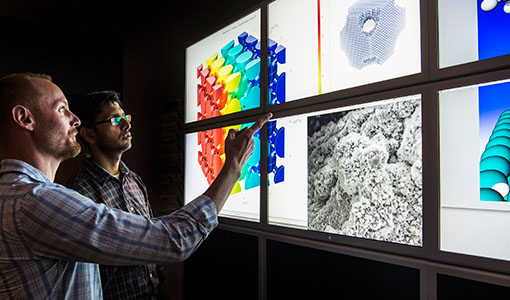 Two researchers facing a wall of computer monitors in a lab.