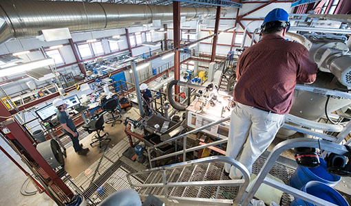 One researcher with safety glasses and a face mask working on equipment in a lab.