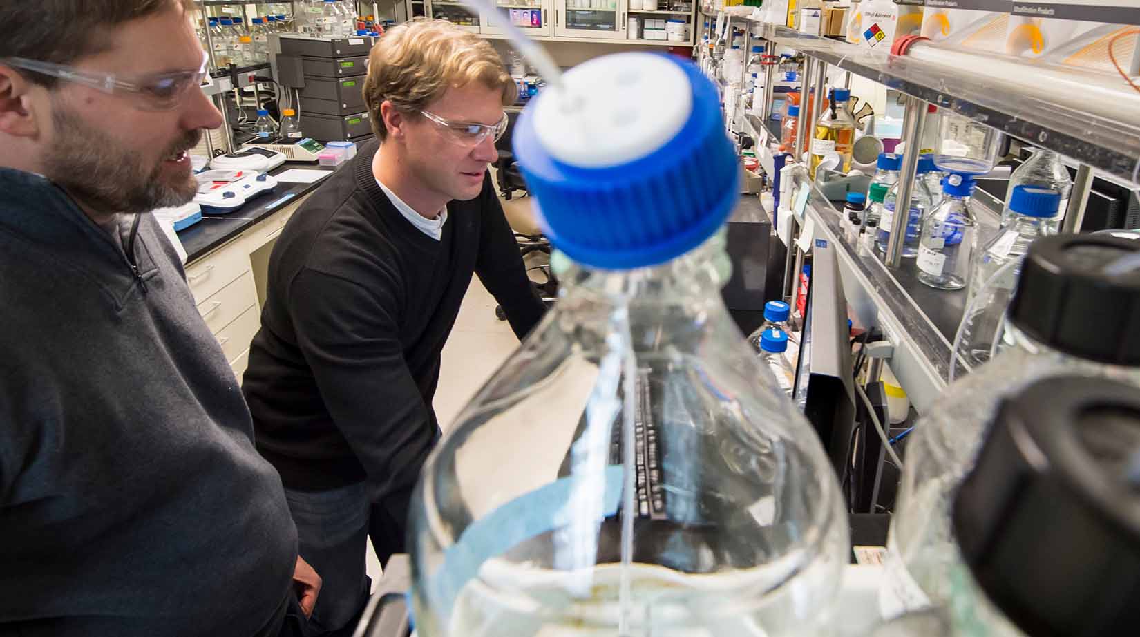 Two researchers in a laboratory with shelves of glass vials.