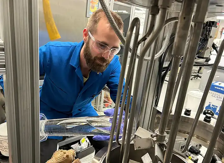 A researcher pours a liquid into a machine in a lab.