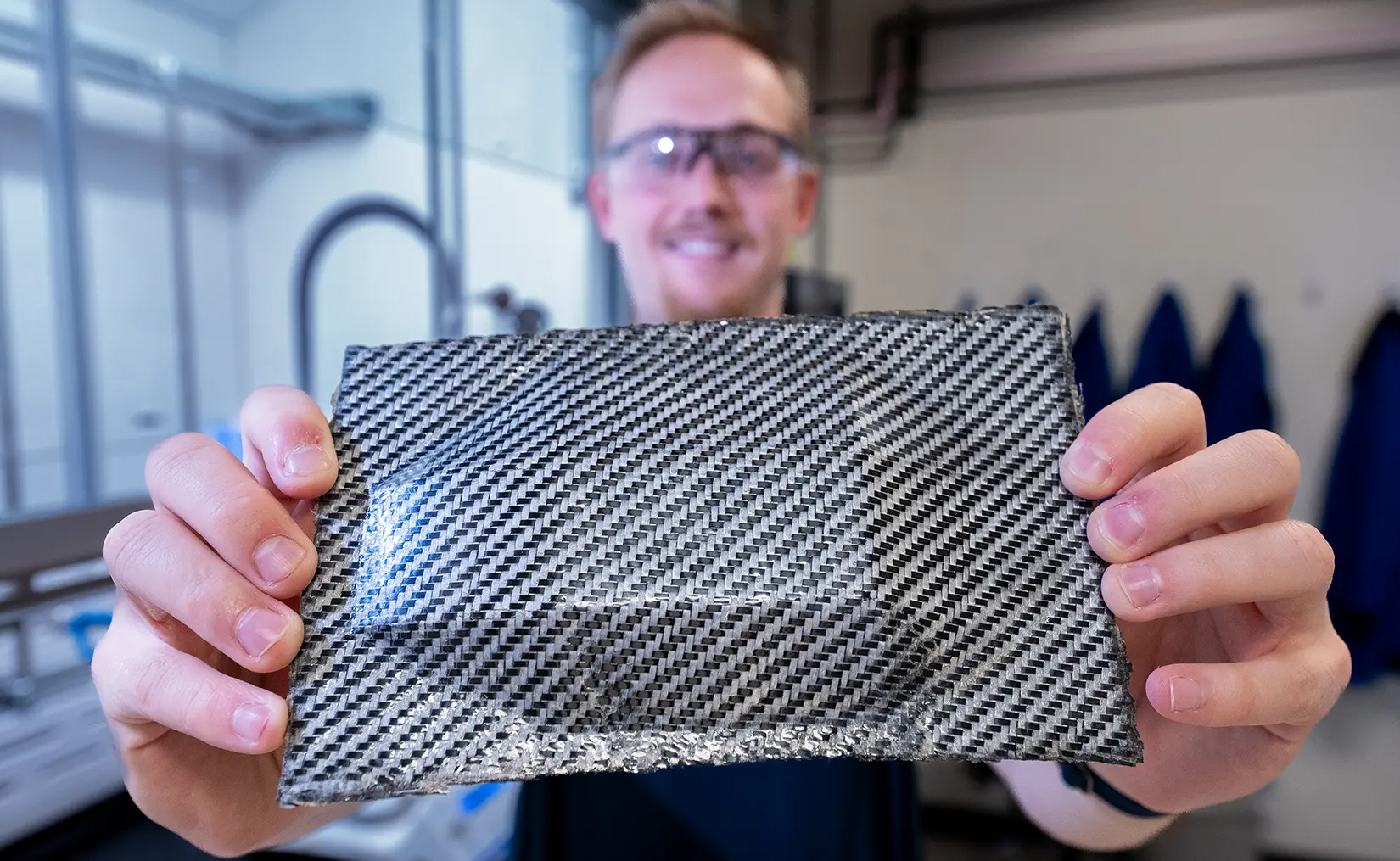 A researcher holds up a hybrid carbon fiber composite with enhanced ductility, utilizing PolyEster Covalently Adaptable Network resin.