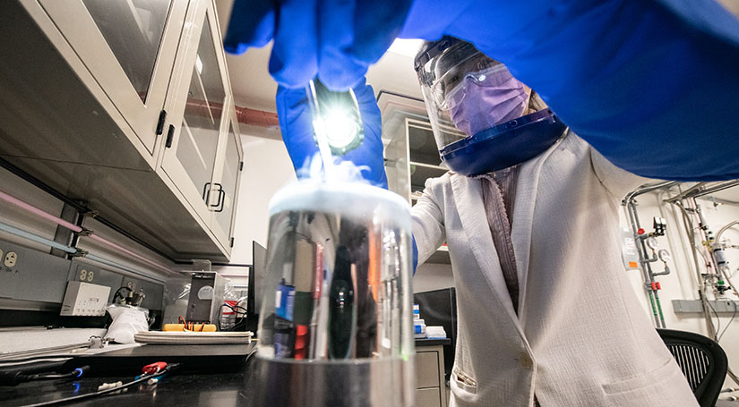 One researcher with safety glasses and a face mask working on equipment in a lab.