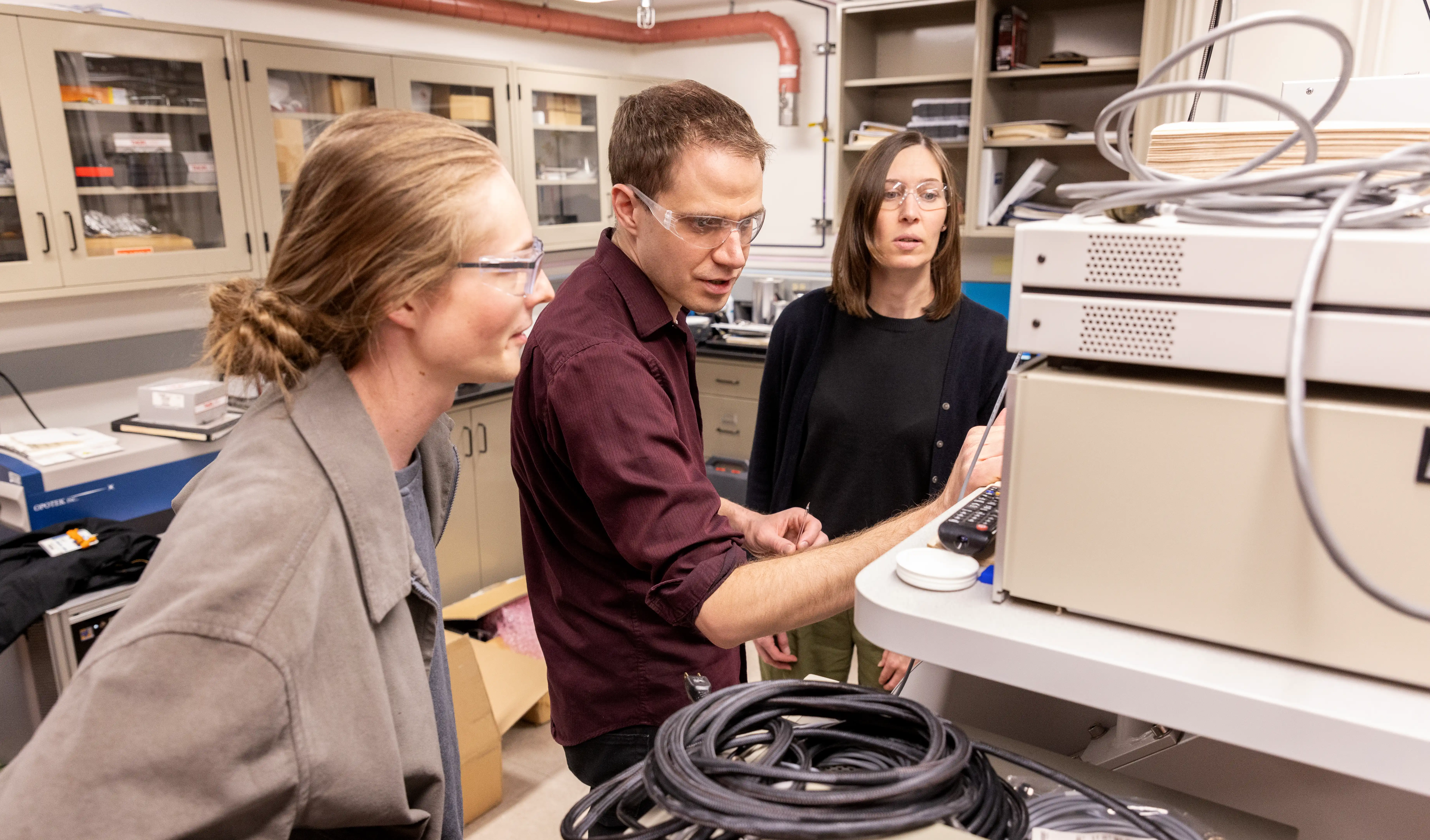 Three researchers discuss the electron paramagnetic resonance spectrometer.