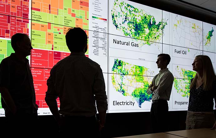 Four people looking at colorful graphics on a large screen.