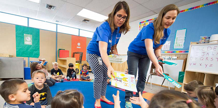 Two  NREL staff members hand out books to children in a classroom.