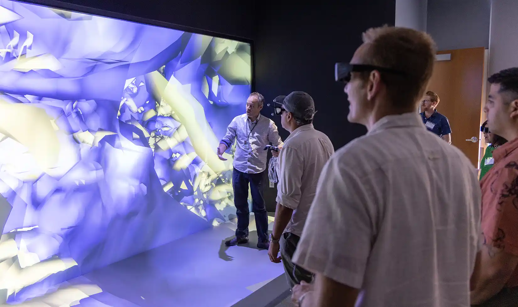 101519-hero A presenter demonstrates an immersive 3D visualization on a large display wall to a group of visitors wearing stereoscopic 3D glasses.