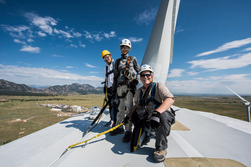 Three people in protective gear pose for a photo atop a wind turbine.