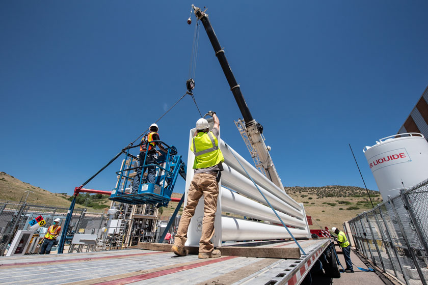 Two people wearing personal protective gear operate construction equipment on a platform.
