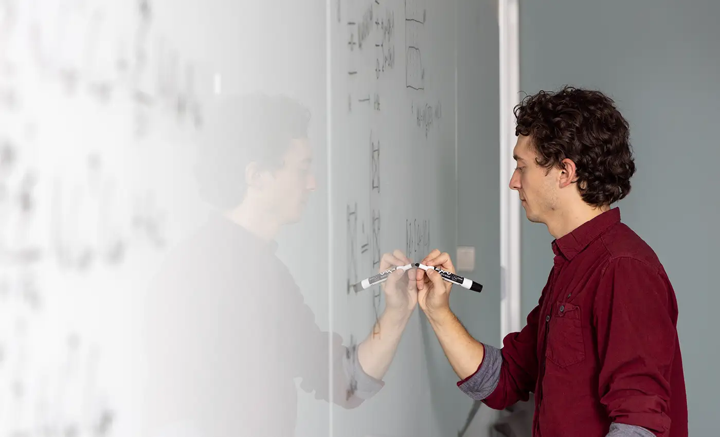Scientist writing on a whiteboard as part of his research process into quantum computing benchmark problems.