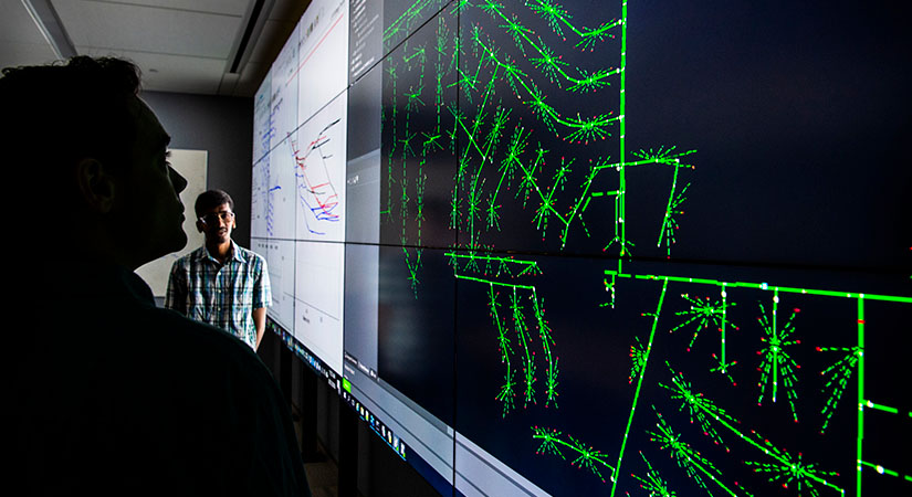 Two researchers view a data visualization display of a multi-timescale simulation for evaluating real-time grid control challenges.
