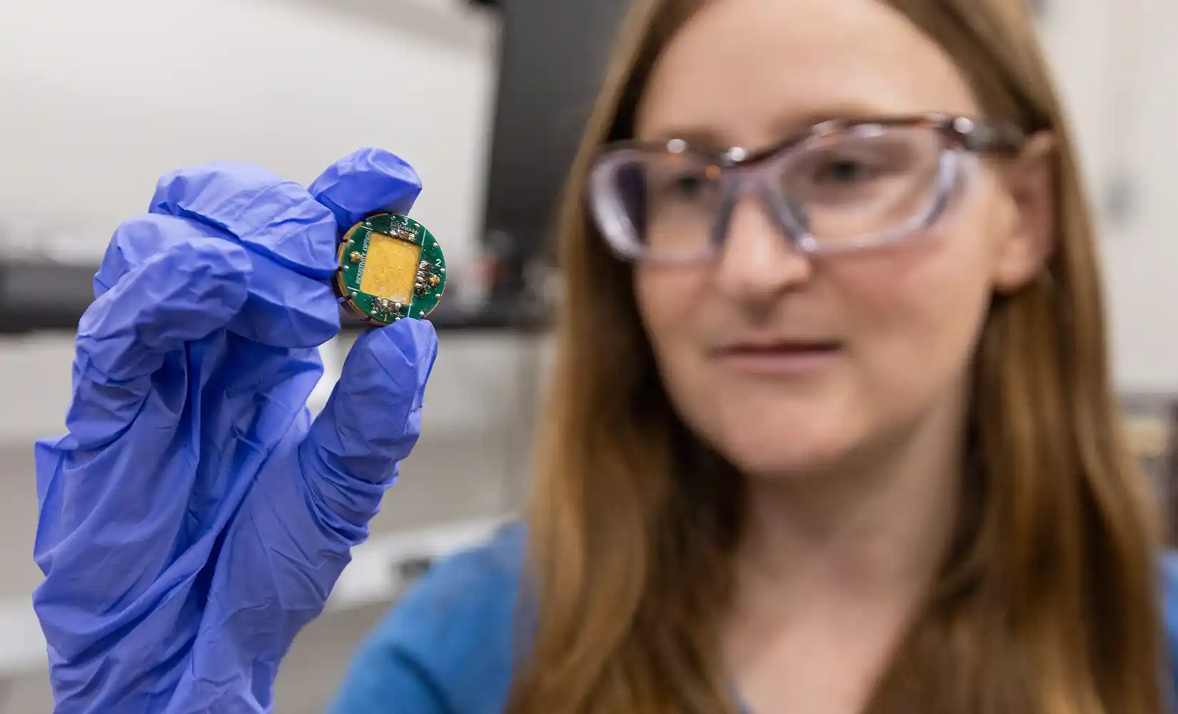 Researcher holds up a sample holder to measure electrical resistivity at low temperature and high magnetic field.
