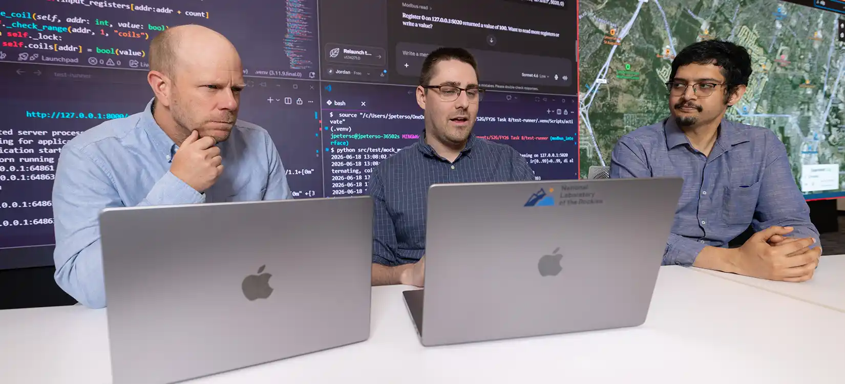 Three cybersecurity researchers look at their laptops with large data screen behind them.