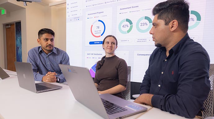 Three researchers sit in front of laptops with dashboard displayed in background