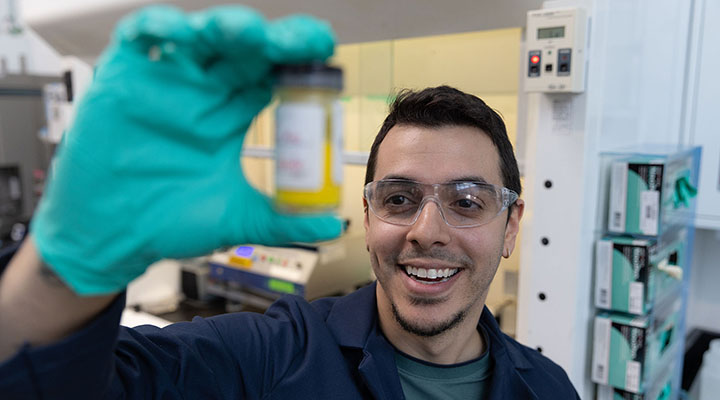 A person wearing gloves holds up a small glass container of liquid.