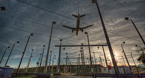 Photo of a large commercial airplane flying over electric infrastructure at an airport.