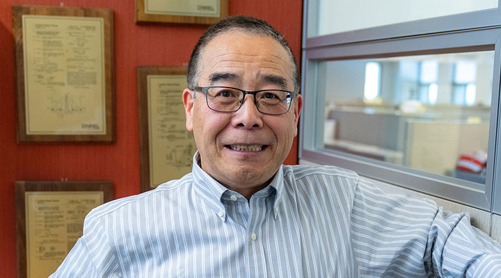 A smiling man poses in front of plaques on a wall.