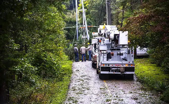 a utility truck and workers assess powerlines on a rural road after a storm