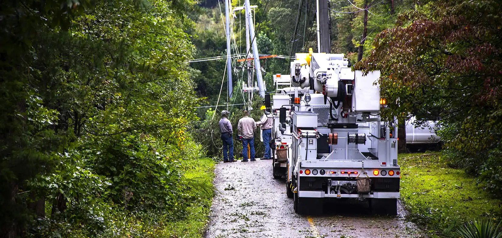 a utility truck and workers assess powerlines on a rural road after a storm