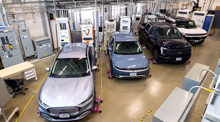 Four cars parked next to chargers inside a laboratory.