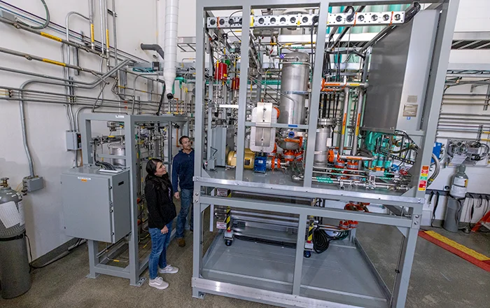 Two people stand inside lab monitoring liquid alkaline electrolyzer equipment