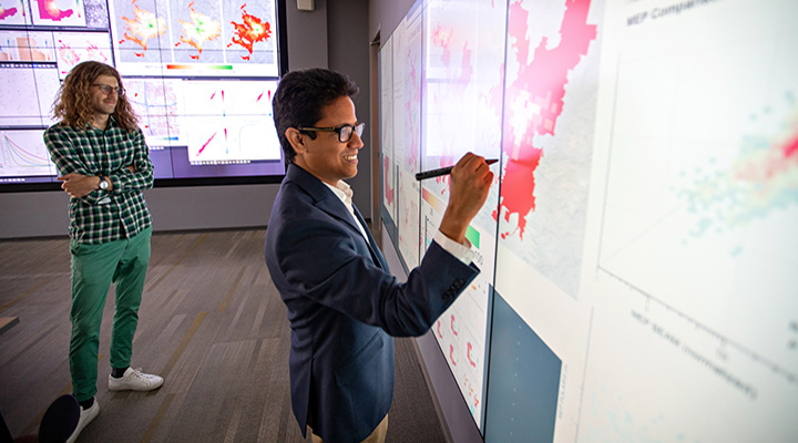 Photo of two researchers looking at large computer display and writing on it