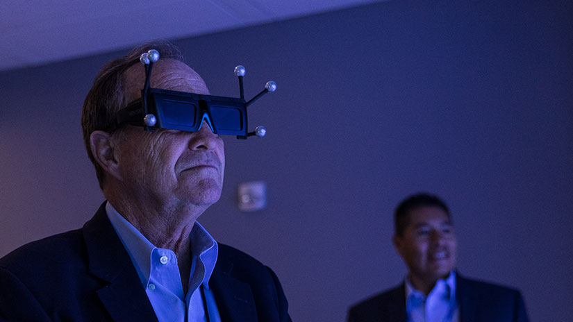 Person wears VR headset while another person in the background watches