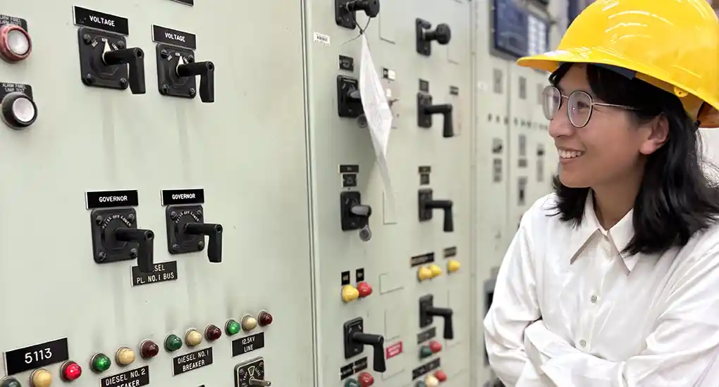 Woman in safety helmet with wall of control switches.