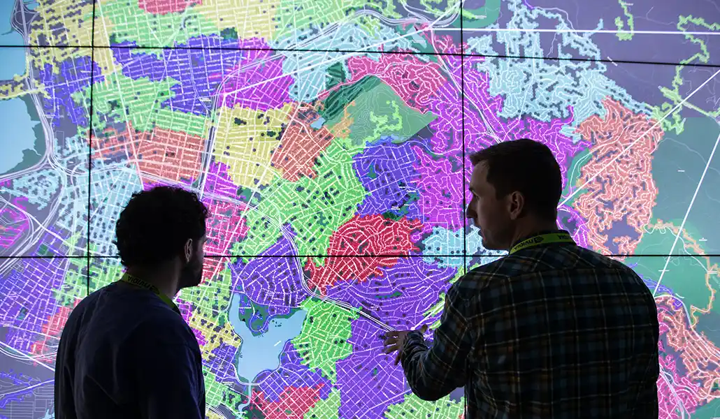 Two people discuss a map projected onto a wall.