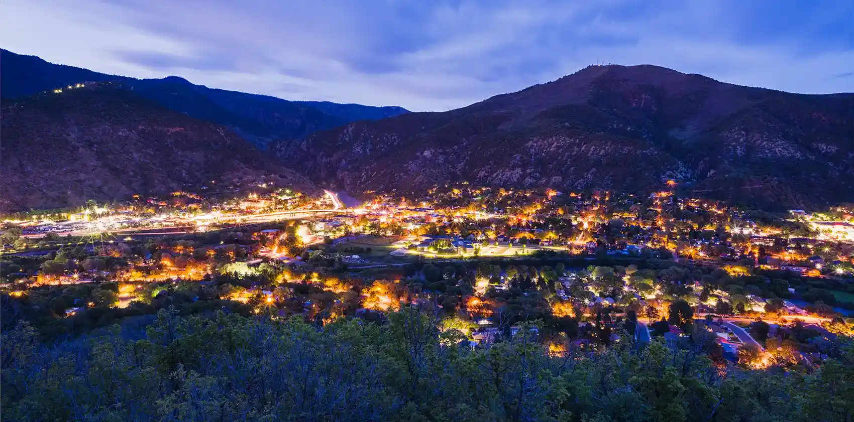 Overlooking town lit up at twilight with mountains in background.