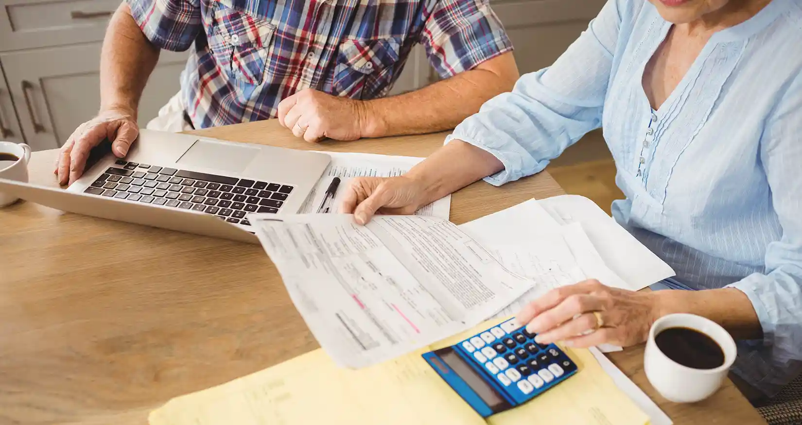 adobestock-104148108-hero Two people look at a laptop and papers with a calculator and coffee mugs on the table.