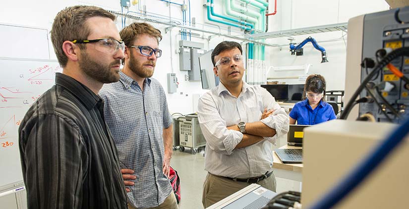 Three researchers examining inverter test waveforms on a computer monitor
