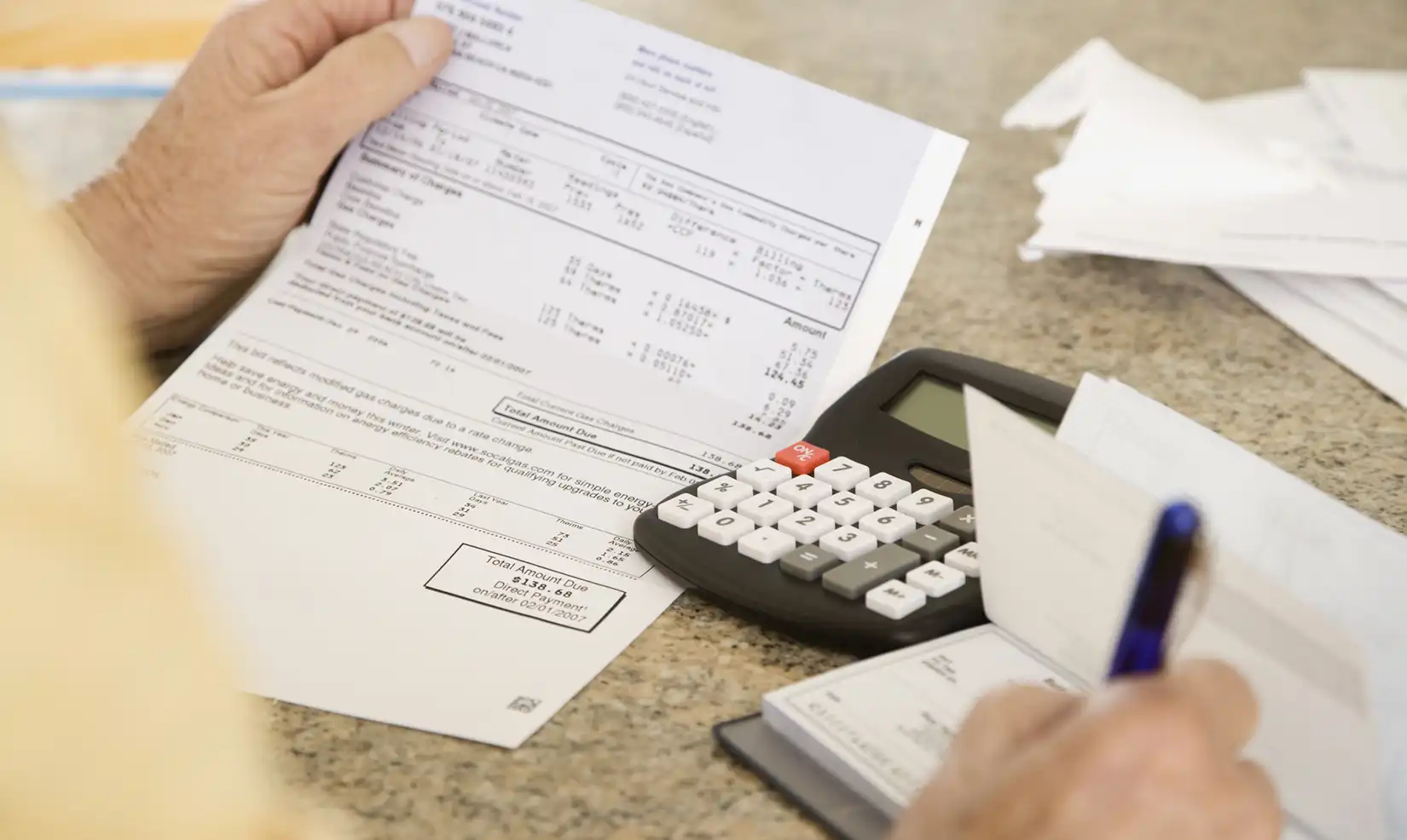 Person holding a utility bill next to a calculator on a table