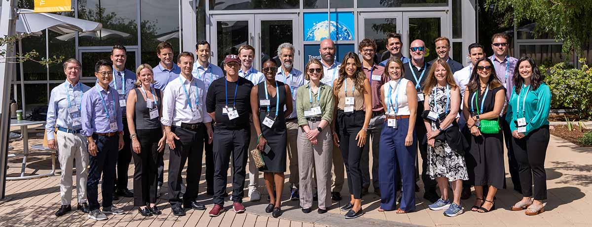 Two rows of 24 people stand in front of a building and pose for a photo.