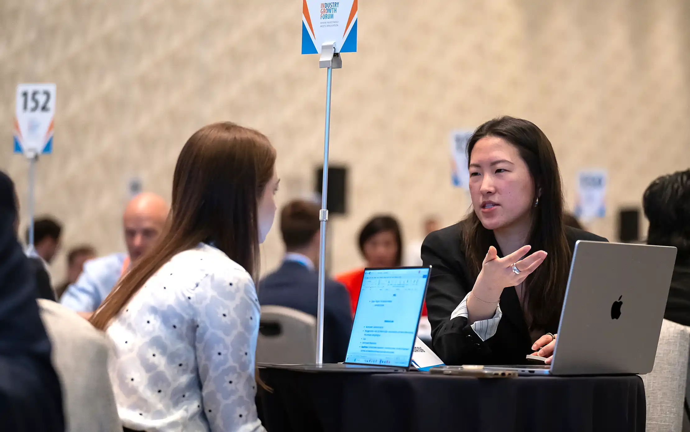 Two people talk at a table in a large meeting room.