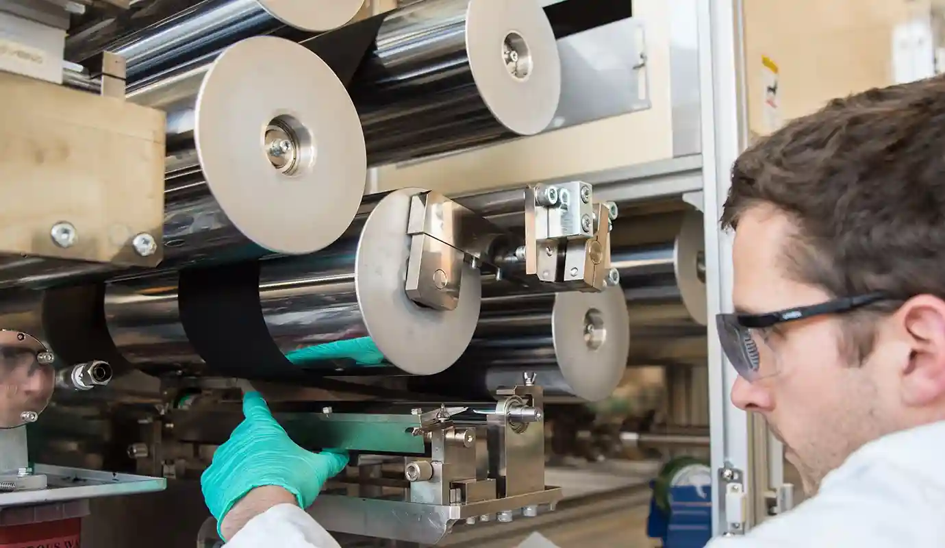 Technician in safety glasses and gloves adjusting a machine in a lab.