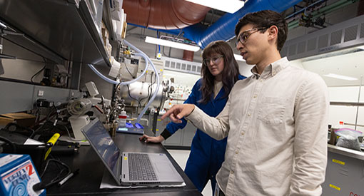Two people look over at laptop inside manufacturing research facility