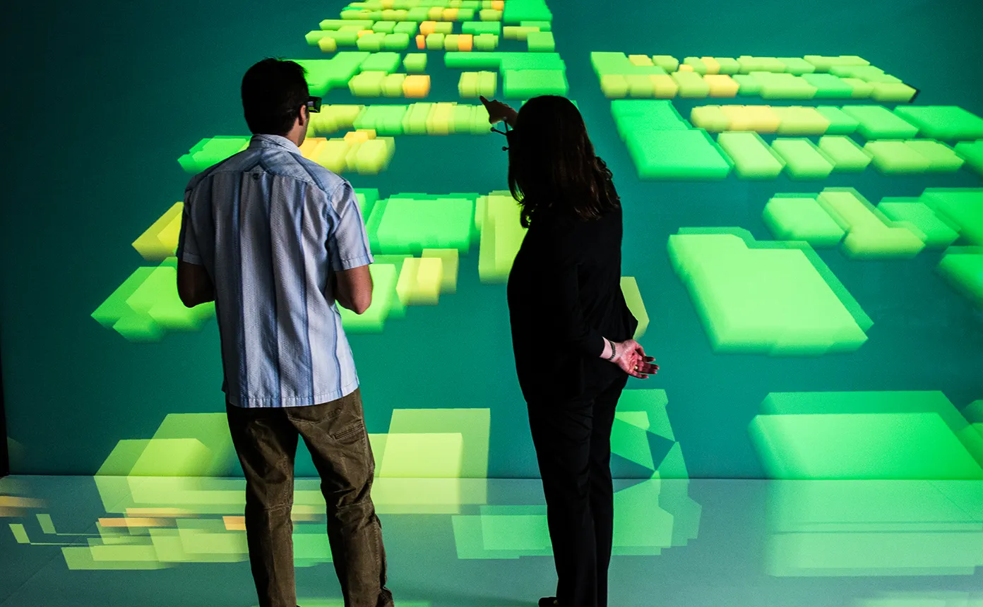 Two people wearing 3D-visualization glasses stand in front of a large screen displaying data in three-dimensional structures.