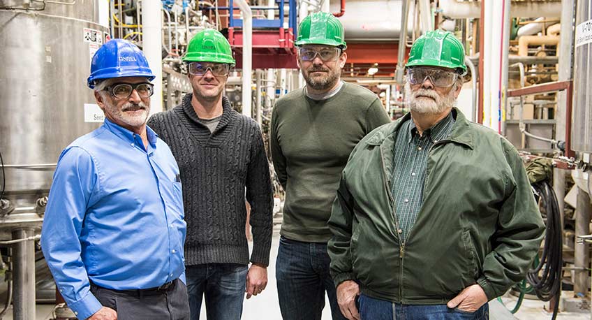Four men stand in front of equipment in a lab at NREL.