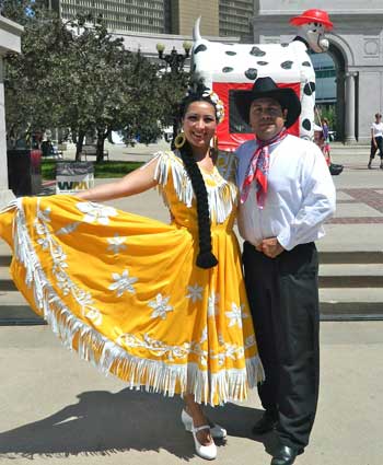A man and a woman in Mexican costumes strike a pose outdoors.