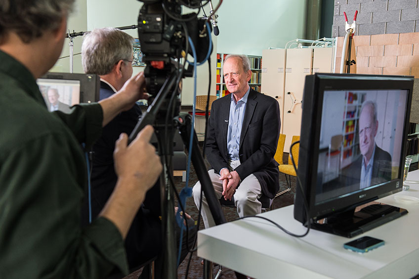 A man sits in front of video cameras and crew