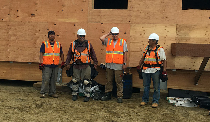 Four men wearing construction gear stand together on a worksite