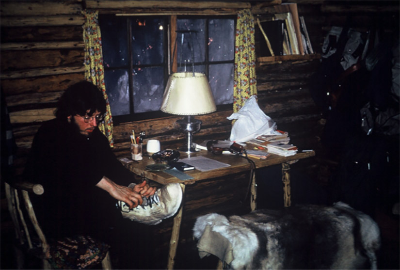 A man takes off snow boots inside of a log cabin